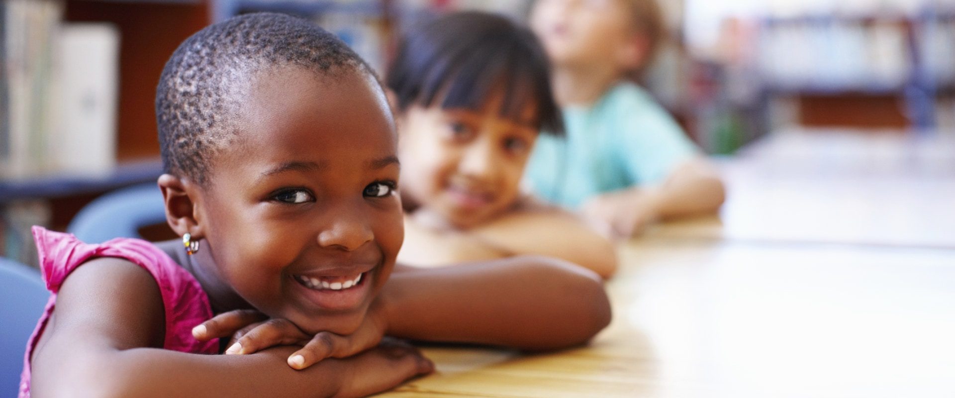 Young children sitting and smiling at their desks.