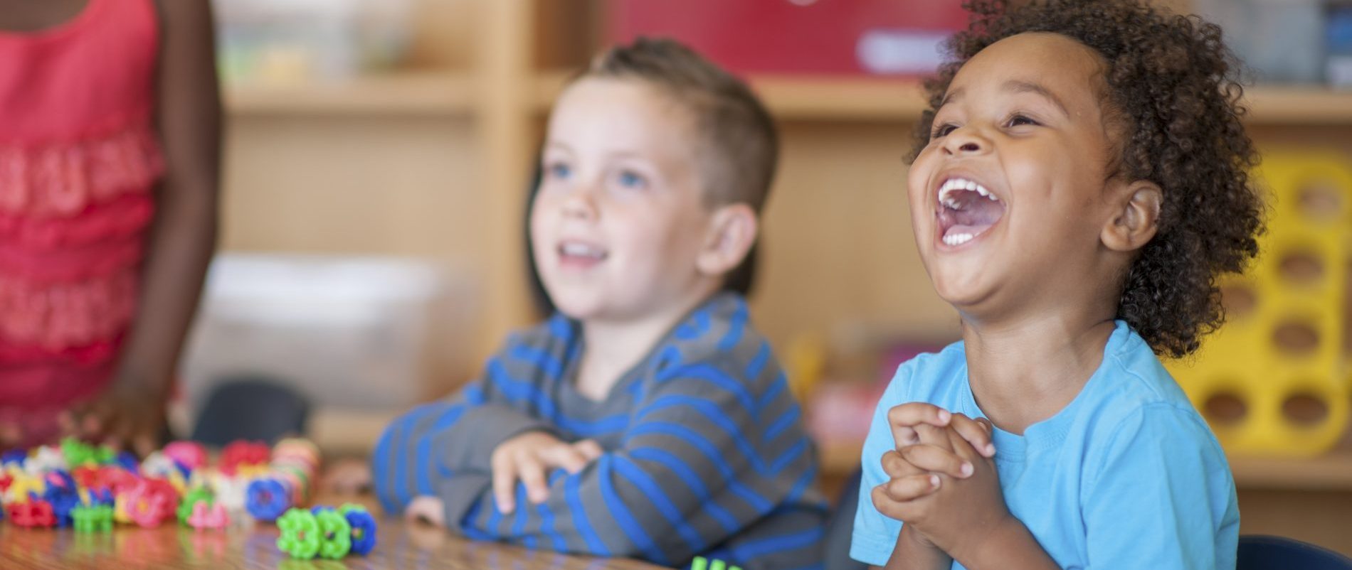 Preschool children are playing with toy blocks and laughing together at a classroom table.