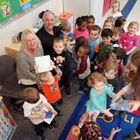 Group of children with teacher in a classroom at a learning center holding up artwork.